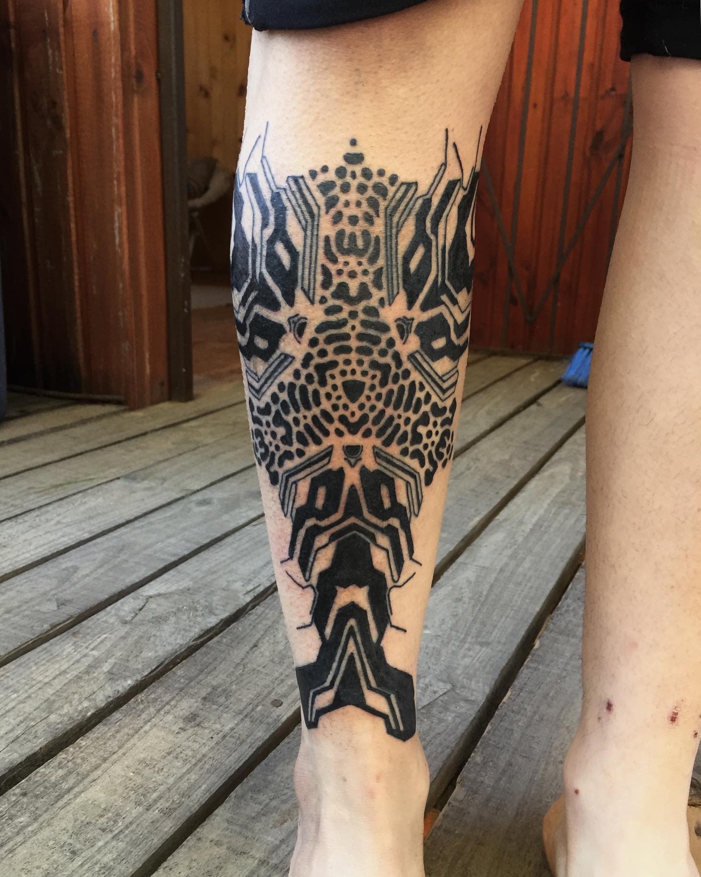 Cyberpunk tattoo on calf featuring an intricate, symmetrical design with geometric and circuit-like patterns in bold black ink